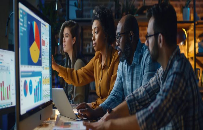 Professionals working together at a computer, reviewing graphs from proposal management software.